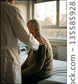 Doctor comforting elderly male patient in hospital room with empathetic care. 135585928