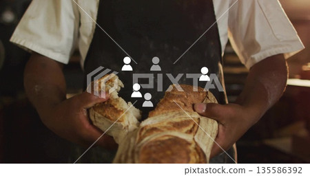 Tearing artisan loaf apart baker wearing apron at wooden countertop in bakery, with warm light 135586392