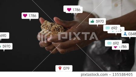 Holding oat and seed cluster, male wearing apron standing in studio kitchen with notification icons 135586405