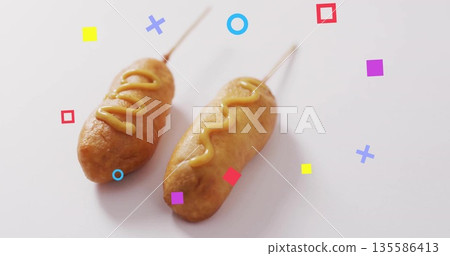 Featuring two battered corn dogs resting on white table, with mustard drizzles and geometric shapes 135586413