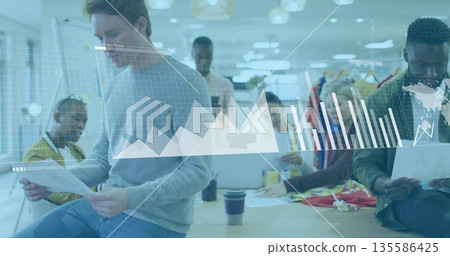 Collaborating six colleagues analyzing digital charts around office table, with laptops and reports 135586425