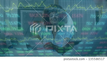 Analyzing female analyst wearing clear glasses monitoring stock tickers on laptop in tech office 135586517
