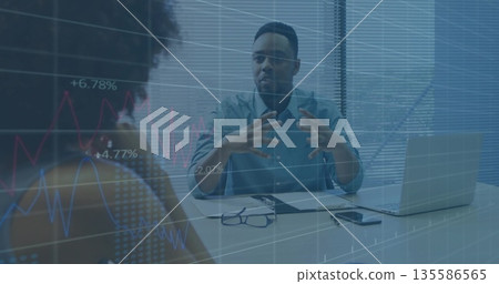 Gesturing man in light blue shirt discussing data at conference desk, with laptop, floating charts Gesturing man in light blue shirt discussing data at conference desk, with laptop, floating charts 135586565