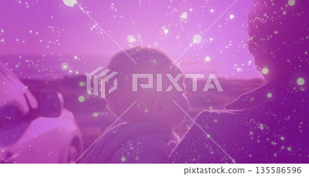 Cradling mother holding baby on rural roadside at sunset, with parked SUV and hooded baby garment 135586596