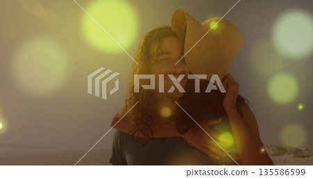 Carrying woman on back, bearded man strolling on sandy shoreline at sunset, with straw sunhat 135586599