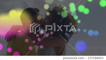 Kissing Black woman and bicultural man embracing at calm shoreline under clear sky, colorful bokeh Kissing Black woman and bicultural man embracing at calm shoreline under clear sky, colorful bokeh 135586603