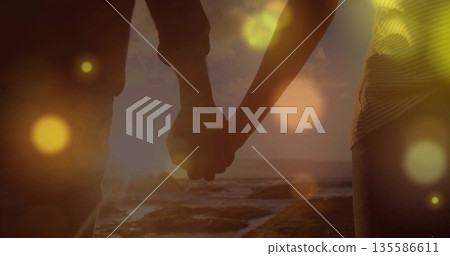 Holding joined hands wearing jeans on rocky beach at sunset, with ocean waves and lens flares 135586611