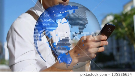 Man wearing white shirt earphones and bag checking smartphone on sunlit sidewalk with globe overlay Man wearing white shirt earphones and bag checking smartphone on sunlit sidewalk with globe overlay 135586634
