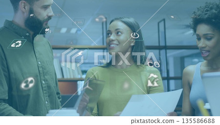 Collaborating colleagues using tablet, papers, laptop at desk with books, eco icons 135586688
