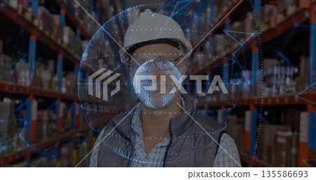 Warehouse worker studying hologram among racks in warehouse, with hard hat safety glasses vest 135586693