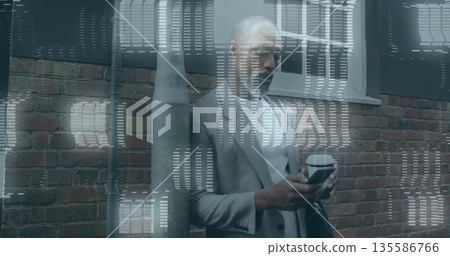 Leaning senior executive wearing suit checking smartphone on city sidewalk, with coffee cup and bag 135586766