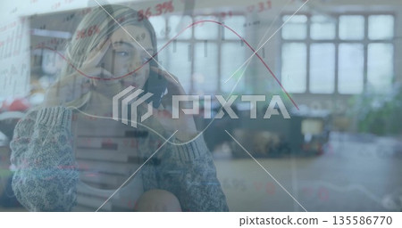 Talking woman in gray sweater, holding smartphone in open-plan office with data overlay, copy space 135586770