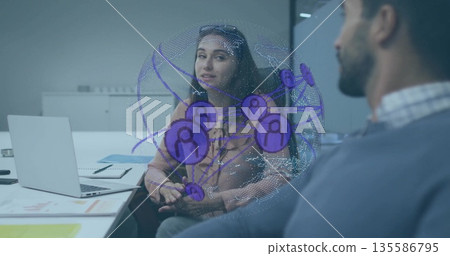 Two coworkers discussing digital network hologram in office meeting room, with laptop and notebook 135586795