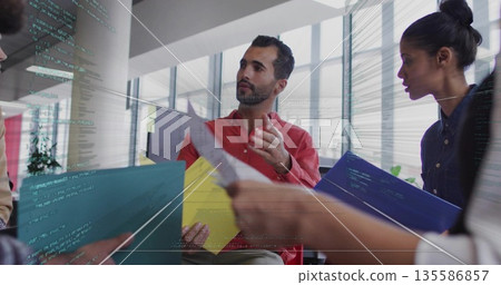 Gesturing red-shirted man discussing project at open office, with colored folders and code overlay Gesturing red-shirted man discussing project at open office, with colored folders and code overlay 135586857