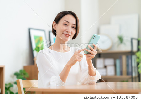 A middle-aged woman watching a smartphone in the living room A middle-aged woman watching a smartphone in the living room 135587003