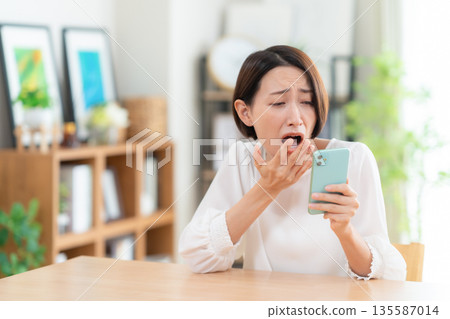 A middle-aged woman watching a smartphone in the living room A middle-aged woman watching a smartphone in the living room 135587014
