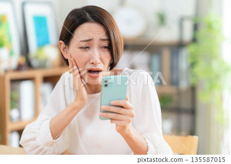 A middle-aged woman watching a smartphone in the living room A middle-aged woman watching a smartphone in the living room 135587015
