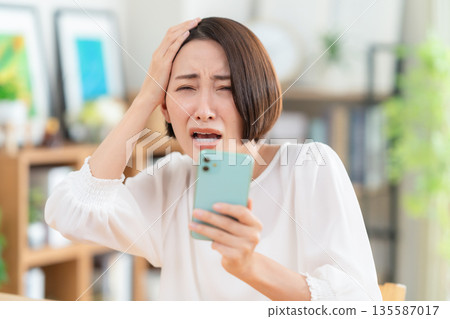 一名中年婦女在客廳裡看著智能手機 135587017