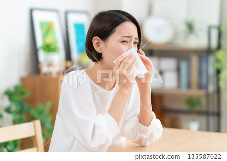 Middle-aged woman blowing her nose in the living room 135587022
