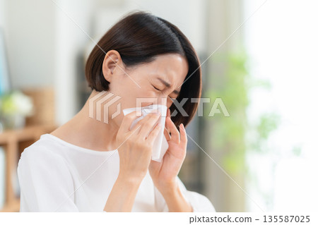 Middle-aged woman blowing her nose in the living room 135587025