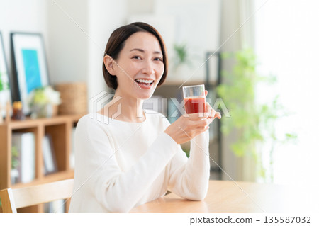 Middle-aged woman drinking tomato juice at home 135587032