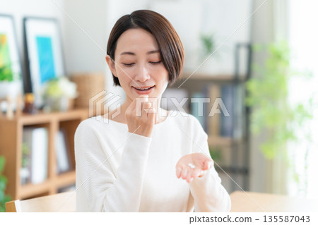 Middle-aged woman taking supplements at home Middle-aged woman taking supplements at home 135587043
