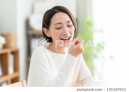 Middle-aged woman eating in the living room Middle-aged woman eating in the living room 135587052