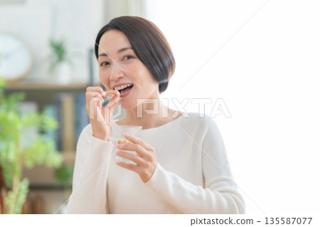 Middle-aged woman taking supplements at home Middle-aged woman taking supplements at home 135587077