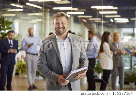 Portrait of smiling business leader or ceo in suit standing in conference room on business meeting. Portrait of smiling business leader or ceo in suit standing in conference room on business meeting. 135587164