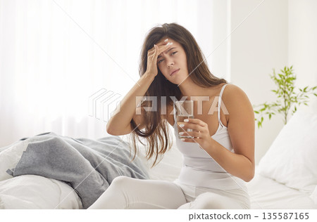 Young upset woman suffering from headache disease sitting on bed in bedroom at home Young upset woman suffering from headache disease sitting on bed in bedroom at home 135587165