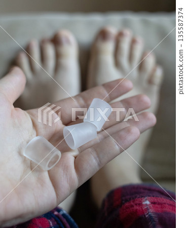 Silicone toe sleeve or cap. Woman puts on protective cover on little toe. Fights corns, prevents blisters and ingrown toenails 135587374