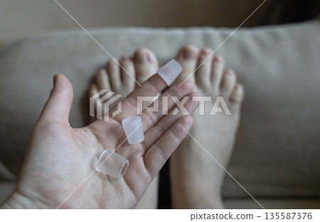 Silicone toe sleeve or cap. Woman puts on protective cover on little toe. Fights corns, prevents blisters and ingrown toenails 135587376