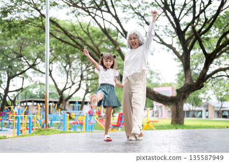 Old woman grandmother holding hand and funny walking with a kid girl granddaughter in park or garden Old woman grandmother holding hand and funny walking with a kid girl granddaughter in park or garden 135587949
