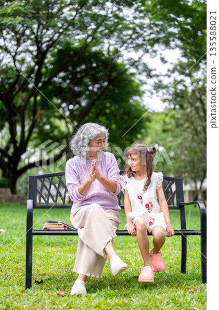 Old woman granny clapping cheering for a kid girl granddaughter after dancing on grass in the park. Old woman granny clapping cheering for a kid girl granddaughter after dancing on grass in the park. 135588021