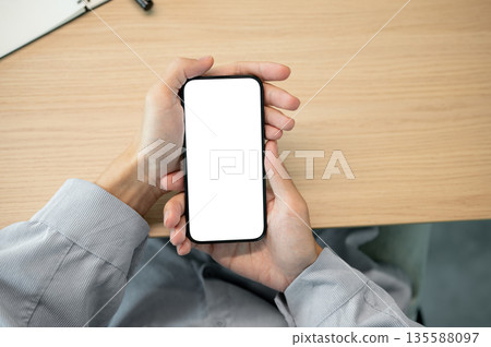 Close up man hand holding blank screen smartphone while sitting at wooden table in a cafe or library Close up man hand holding blank screen smartphone while sitting at wooden table in a cafe or library 135588097