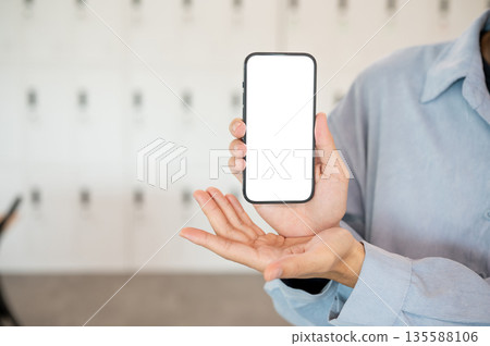 Close up of a man holding and showing a white screen smartphone while standing in cafe or classroom Close up of a man holding and showing a white screen smartphone while standing in cafe or classroom 135588106