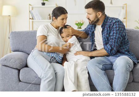 Worried parents comforting sad child on couch during family crisis at home 135588132