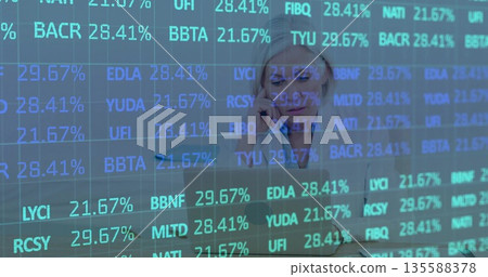 Focusing financial analyst balancing smartphone and laptop in office, with live market data overlay 135588378