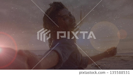 Spinning woman holding smartphone on sunset beach in long sleeves, with lens flare, grain overlay Spinning woman holding smartphone on sunset beach in long sleeves, with lens flare, grain overlay 135588531