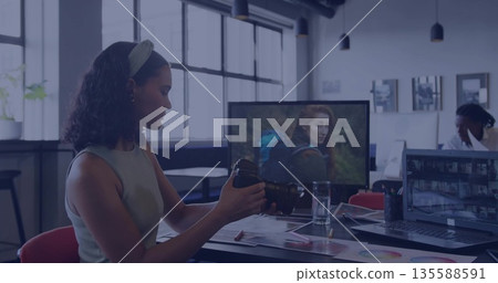 Inspecting woman in green top adjusting DSLR lens at office desk, with laptop, chart, copy space 135588591