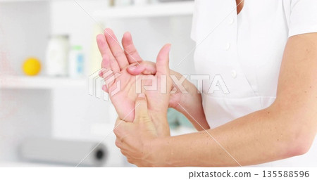 Therapist in uniform pressing forearms kneading client open palm at spa with shelving and towel Therapist in uniform pressing forearms kneading client open palm at spa with shelving and towel 135588596