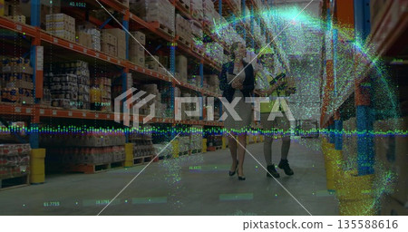 Inspecting orange shelving with boxes in warehouse, women wearing helmets and vest carrying tablets 135588616