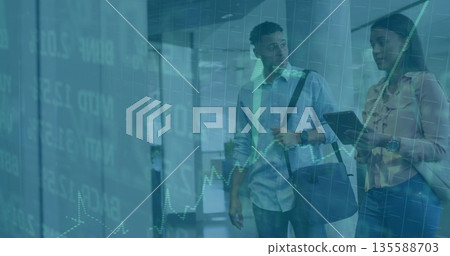 Coworkers in business attire analyzing chart overlay in office hallway, with tablet, messenger bag Coworkers in business attire analyzing chart overlay in office hallway, with tablet, messenger bag 135588703