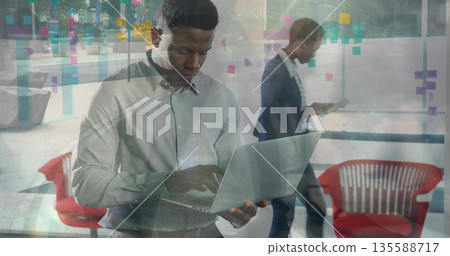Typing man in button-up shirt on laptop in office, with tablet and sticky notes, copy space Typing man in button-up shirt on laptop in office, with tablet and sticky notes, copy space 135588717