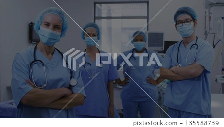 Standing surgical team wearing light blue scrubs in operating room, with stethoscopes and monitors Standing surgical team wearing light blue scrubs in operating room, with stethoscopes and monitors 135588739
