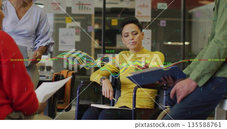 Analyzing woman in yellow sweater pointing at report in open-plan office, with laptop and charts Analyzing woman in yellow sweater pointing at report in open-plan office, with laptop and charts 135588761