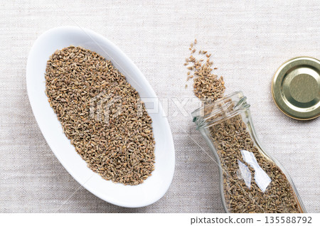 Aniseed, anise seeds, in white bowl on linen. Anise fruits, mistakenly called seeds, from the plant Pimpinella anisum, used to flavor food, candy, and alcoholic drinks, around the Mediterranean. Photo 135588792