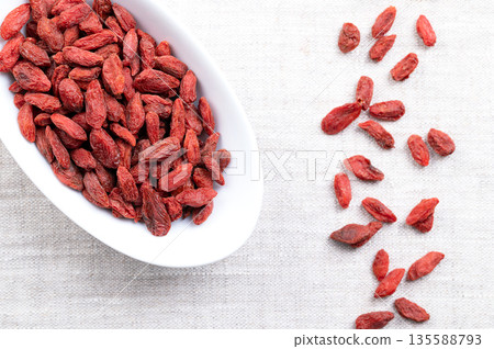Goji berries, dried fruits in white bowl on linen. Also Chinese wolfberry, red medlar, and matrimony vine. Bright, orange-red, sweet fruits of Lycium barbarum, native to China and across Asia. Photo 135588793
