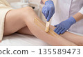 Waxing treatment happening in a beauty salon with a person getting hair removal on their leg 135589473