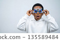 Child in white sweater looks surprised while wearing vision testing glasses indoors at an eye exam office 135589484